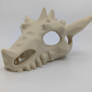 Könnte beinhalten: Ein beigefarbener, 3D-gedruckter Drachenschädel mit einer detaillierten, strukturierten Oberfläche. Der Schädel hat eine große Augenhöhle und eine spitze Schnauze.