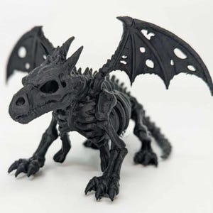 Op de afbeelding: Een zwart draak skelet beeldje met gedetailleerde ribbenkast, ruggengraat en klauwpoten. De draak heeft grote, geperforeerde vleugels en een schedelachtig hoofd met zichtbare oogkassen. Het beeldje staat in een viervoetige houding.