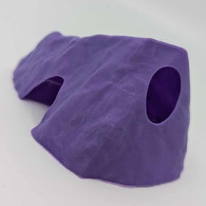 以下が含まれることがあります： 2つの開口部のある紫色のプラスチック製の洞窟。洞窟は岩のように見えるようにテクスチャ加工されています。