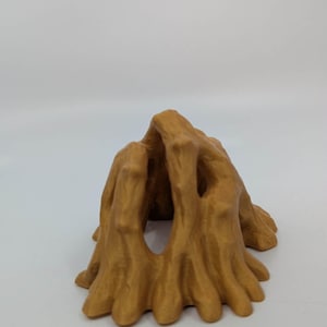 May include: A golden-brown, abstract sculpture resembling a tree trunk or cave entrance. The object has a textured surface with multiple openings and a rounded, organic shape. The sculpture is set against a plain white background.