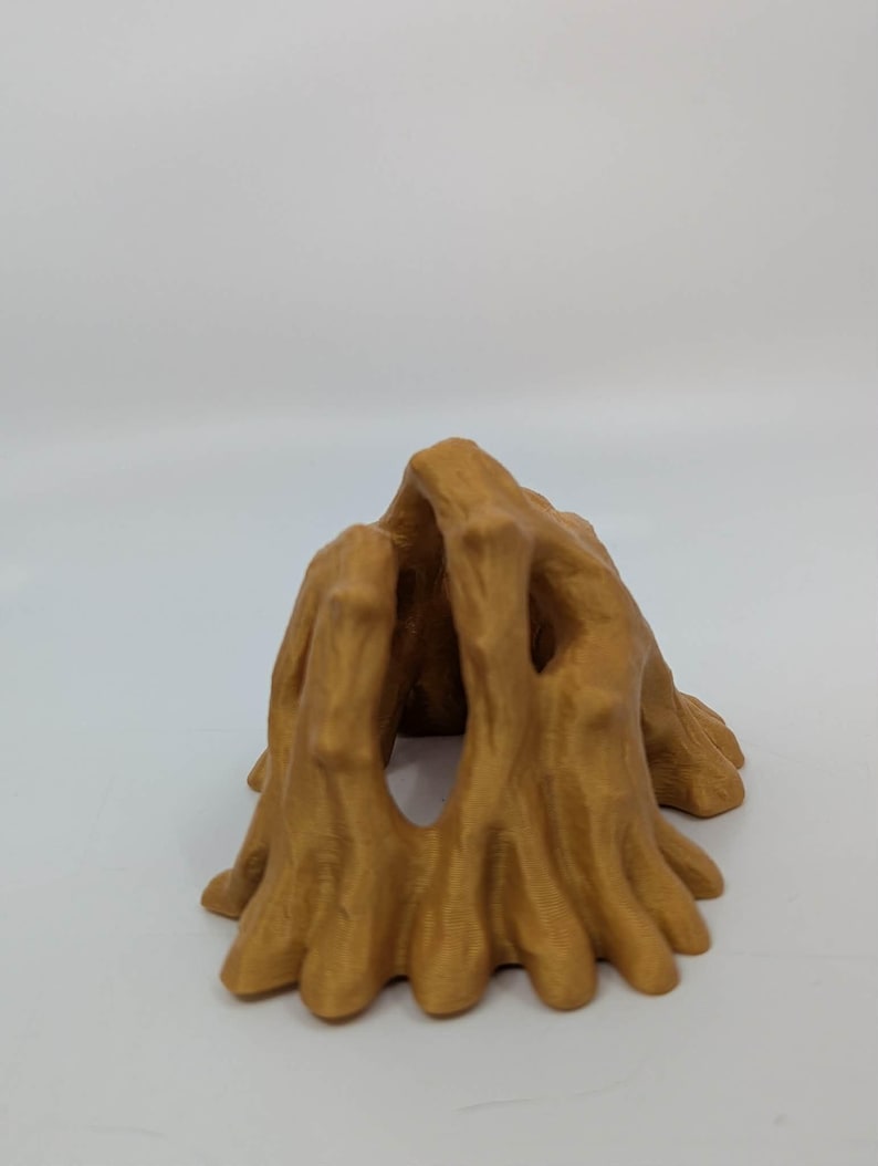 May include: A golden-brown, abstract sculpture resembling a tree trunk or cave entrance. The object has a textured surface with multiple openings and a rounded, organic shape. The sculpture is set against a plain white background.