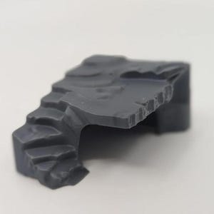 May include: A grey plastic miniature rock formation with steps and a flat surface. The rock has a textured appearance, designed for model building or tabletop gaming. The steps lead up to a flat platform.
