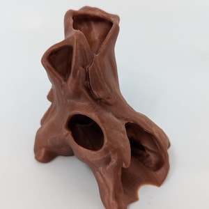 Może przedstawiać: Brązowa rzeźba w kształcie drzewa o teksturowanej powierzchni i wielu otworach. Organiczna forma ma szorstki, przypominający korę wygląd, z wydrążonym środkiem i kilkoma nieregularnymi otworami. Rzeźba jest prawdopodobnie wykonana z litego materiału.