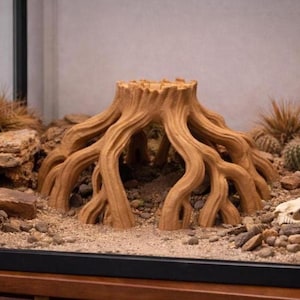 May include: A brown artificial tree root ornament for an aquarium or terrarium. The textured design mimics natural wood, with multiple root-like structures extending outwards. The ornament is surrounded by sand and small rocks.