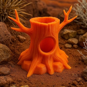 May include: An orange tree stump-shaped container with a hollowed-out center and a circular opening. The container has branches extending from the top and is set on a textured surface with rocks and plants.