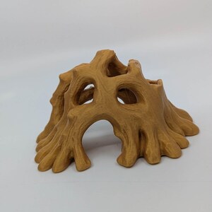 May include: A 3D-printed, tan-colored tree stump with multiple openings and a textured surface. The design features a hollowed-out center and detailed, organic shapes, suitable for decorative purposes or as a small animal habitat.