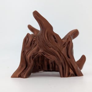 Può includere: Scultura di ceppo d'albero stilizzata, marrone, con superficie strutturata. La scultura presenta molteplici rami rivolti verso l'alto e un centro scavato. Il colore è un marrone caldo e ricco, e il design ricorda il legno naturale.