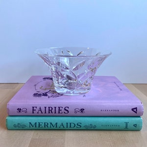 May include: A clear glass bowl with a decorative pattern sits on top of two books. The top book is lavender and says "The Fairies" by Alexander. The bottom book is teal and says "Mermaids" by Alexander.