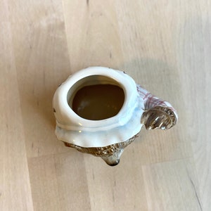 May include: A ceramic mug shaped like a brown bear wearing a white and red checked scarf. The mug is empty and the inside is visible.