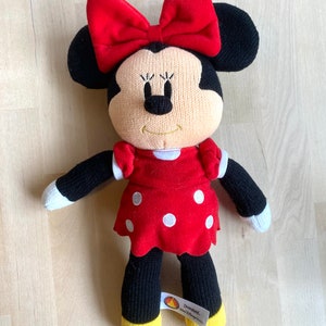 May include: Knitted Minnie Mouse plush toy wearing a red dress with white polka dots and a red bow. The toy has a yellow tag that says "Disneyland."