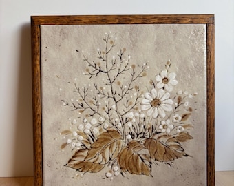 May include: Square ceramic tile with a floral design in a wooden frame. The artwork features brown and white flowers, leaves, and berries on a beige background. The wooden frame is a medium brown color.