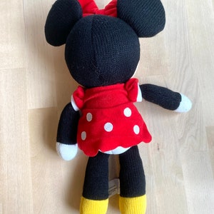 May include: A black and red knitted Minnie Mouse plush toy with white polka dots on her red dress. She has large black ears and a red bow.