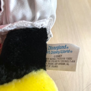 以下が含まれることがあります： 白レースのトリムとディズニーランドのタグが付いた黒と黄色のぬいぐるみ。タグには「Disneyland&reg; Walt Disney World&reg; &copy;DISNEY NEW MATERIALS POLYESTER FIBERS 5:PA 1378:OHIO PA 1378 HASS 1-616 A TRADING CORP. BURBANK, CA, CT OF SRILANKA」と記載されています。