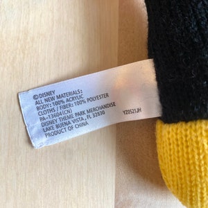 May include: A white tag with black text that reads "&copy;DISNEY ALL NEW MATERIALS: BODY: 100% ACRYLIC CLOTHS/FIBER: 100% POLYESTER PA-13604(CN) DISNEY THEME PARK MERCHANDISE LAKE BUENA VISTA, FL 32830 PRODUCT OF CHINA YZ0521JH"