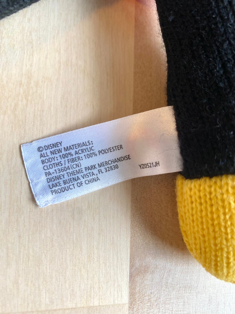 May include: A white tag with black text that reads "&copy;DISNEY ALL NEW MATERIALS: BODY: 100% ACRYLIC CLOTHS/FIBER: 100% POLYESTER PA-13604(CN) DISNEY THEME PARK MERCHANDISE LAKE BUENA VISTA, FL 32830 PRODUCT OF CHINA YZ0521JH"