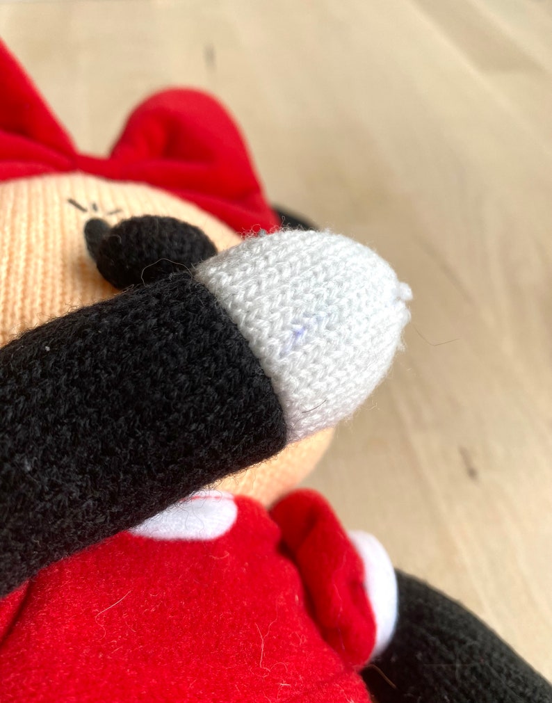 May include: A knitted plush toy of a cartoon character wearing a red dress, black arms, and a white face. The toy has a red bow on its head and a white glove on one hand.