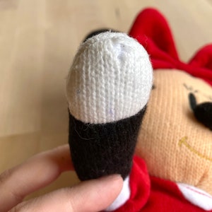 May include: A red and white plush toy with a black nose and a white knitted hat. The toy is missing some of the white knit on the hat.