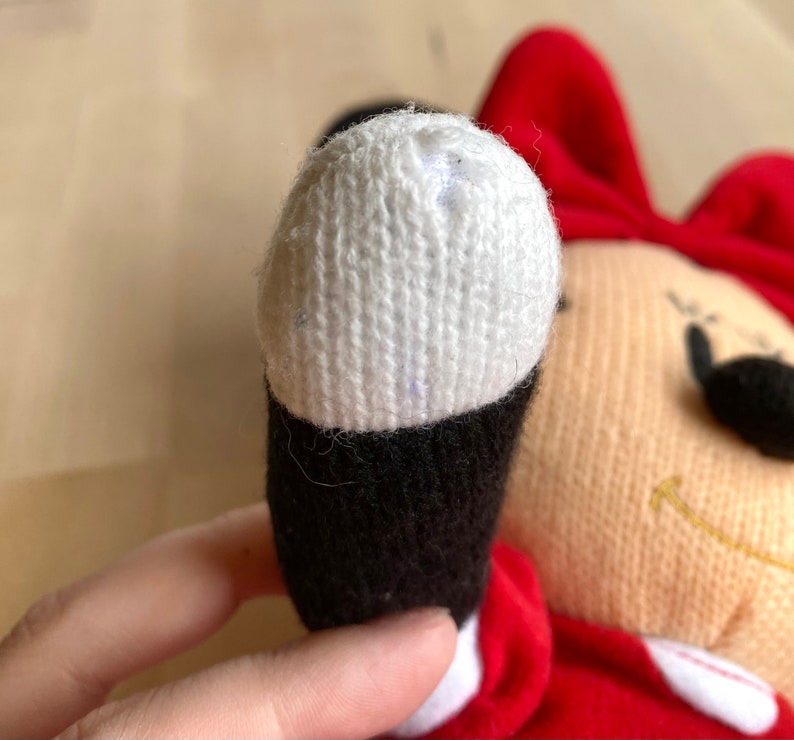 May include: A red and white plush toy with a black nose and a white knitted hat. The toy is missing some of the white knit on the hat.