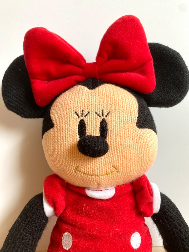 May include: A plush toy of Minnie Mouse wearing a red dress with white polka dots and a red bow. She has black ears and a black nose.