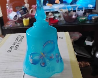 Puede incluir: Una campana de cristal azul brillante translúcido con un diseño de mariposa pintado a mano en tonos azules, amarillos y blancos. La campana tiene un mango liso y redondeado y un borde inferior acampanado y festoneado.