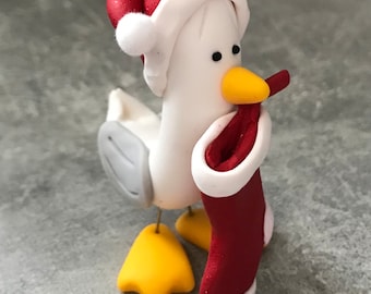 以下が含まれることがあります： サンタ帽をかぶり、クリスマスストッキングを持ったカモメの気まぐれな置物。カモメは白で、灰色の翼、黄色の足、黄色のくちばしがあります。サンタ帽とストッキングは赤と白のトリムで、休日の装飾に最適です。