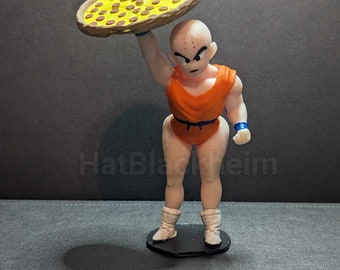 May include: A bald, orange-clad figurine with a serious expression holds a pizza above its head. The pizza has a yellow crust and red pepperoni toppings.