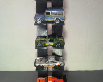 May include: A black, multi-tiered display shelf holding five toy cars. The cars are various colors, including red, blue, green, silver, and orange. The shelf is made of black material and is designed to showcase the toy cars.