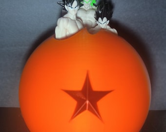 May include: Three black and green anime figurines are perched on top of an orange dragon ball with a red star.