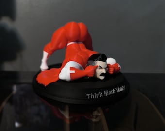 May include: A figurine of a superhero in a red and white costume, bent over with his head resting on a black base. The base has the text "Think Mark Think!" in white.