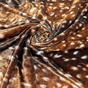May include: Close-up of a fabric with a deer fur pattern. The fabric features a brown and white spotted design, with shades of brown and tan. The fabric is folded and draped, showing the texture and pattern.