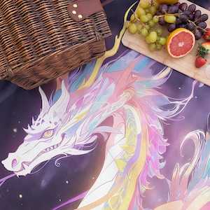 Puede incluir: Una manta de picnic con un drag&oacute;n blanco con una melena y acentos coloridos. El drag&oacute;n se encuentra sobre un fondo p&uacute;rpura oscuro con un efecto de estrellas. Tambi&eacute;n se ven una cesta de mimbre y una tabla de madera con fruta.