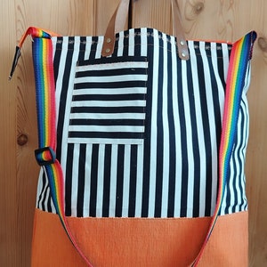 Könnte beinhalten: Tragetasche mit schwarz-weißem Streifenmuster, orangefarbenem Boden und Regenbogenriemen. Die Tasche hat braune Ledergriffe und eine kleine Tasche mit weißen Streifen.
