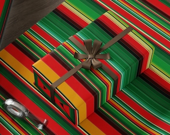 Puede incluir: Un rollo de papel de regalo a rayas verdes, rojas y amarillas con una caja de regalo a juego envuelta en el mismo papel. La caja de regalo está atada con una cinta marrón y un lazo. Hay un par de tijeras y un rollo de cinta adhesiva en la mesa.