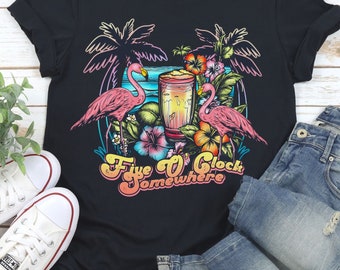 May include: Black t-shirt featuring a graphic of pink flamingos, palm trees, and a tropical drink. The text "Five O'Clock Somewhere" is printed in a retro font.