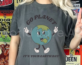May include: A dark gray t-shirt with a cartoon image of a smiling Earth with arms and legs. The text "Go Planet" is above the Earth and "It's Your Earth Day" is below the Earth.