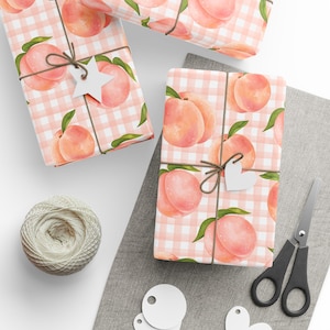 May include: Pink and white gingham wrapping paper with a watercolor peach design. The paper is wrapped around a gift box with a brown twine bow and a white star-shaped tag.