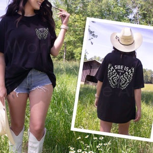 May include: Black oversized t-shirt with a white graphic of angel wings and the text "She is Fierce &" on the back. The front of the shirt has a smaller version of the graphic on the left side of the chest.