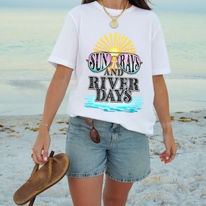 Puede incluir: Camiseta blanca con un gráfico de gafas de sol con una puesta de sol detrás y el texto "Sun Rays and River Days".