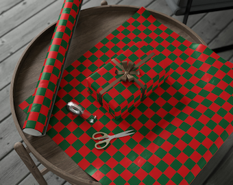 May include: A wrapped present with a brown ribbon, scissors, and a roll of red and green chequered wrapping paper on a wooden table. The wrapping paper is also spread out on the table. A roll of tape is also on the table.