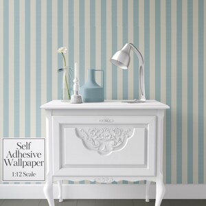 以下が含まれることがあります： 装飾的な彫刻と曲線的な脚を持つ白いナイトスタンド。銀色のデスクランプ、青い花瓶、花が入った透明なガラス瓶が置かれています。背景は青と白のストライプの壁紙です。「Self Adhesive Wallpaper 1:12 Scale」の文字。