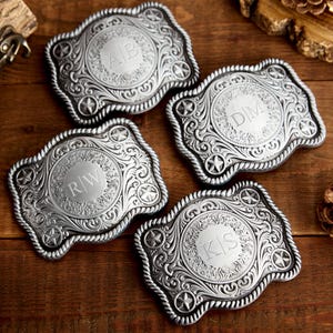 May include: Four silver belt buckles with ornate designs and engraved initials. Each buckle features a star design and a circular center with initials.