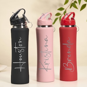 May include: Three personalized water bottles in black, pink, and red. Each bottle has a name in a cursive font: Houston, Kristina, and Brenda. The bottles have a flip-top lid and a silver ring for attaching to a bag.