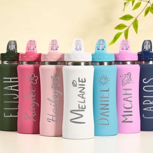May include: A collection of personalized water bottles in various colors, including green, pink, light pink, white, blue, and navy. Each bottle features a name in a stylish font, with some also displaying decorative elements like a flower, butterfly, sun, and planet.