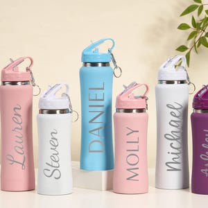May include: A collection of personalized water bottles in various colors, including pink, white, blue, and purple. Each bottle features a name in a stylish font. The bottles have a flip-top lid and a silver carabiner clip.