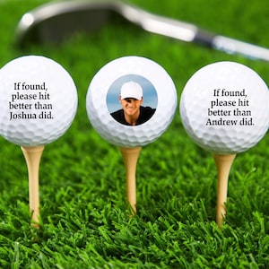 May include: Three white golf balls with personalised messages. The middle ball has a photo of a man wearing a white baseball cap. The left ball says "If found, please hit better than Joshua did." The right ball says "If found, please hit better than Andrew did."