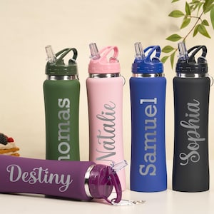 May include: A collection of personalized water bottles in various colors, including green, pink, blue, and black. Each bottle features a name in a stylish font. A purple bottle is lying down in front of the others. The bottles have a straw lid.