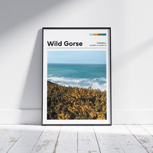 Könnte beinhalten: Ein gerahmter Druck mit schwarzem Rahmen und weißem Hintergrund. Der Druck zeigt ein Foto einer Küstenlandschaft mit gelben Wildblumen im Vordergrund und blauen Ozeanwellen im Hintergrund. Der Text "Wild Gorse" und "Cornwall 50.23867° N, 5.22037° W" ist oben auf dem Druck in Schwarz gedruckt.