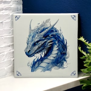 Puede incluir: Azulejo de cerámica azul y blanco con una ilustración detallada de la cabeza y el cuello de un dragón. El dragón está mirando hacia la izquierda y tiene un cuerpo blanco con escamas azules y un fondo azul.
