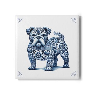 Op de afbeelding: Vierkante keramische tegel met een blauw-wit bulldog-ontwerp. De bulldog is versierd met bloempatronen en krullen. De tegel heeft een witte achtergrond met decoratieve blauwe hoekaccenten. Het ontwerp doet denken aan Delfts blauw.