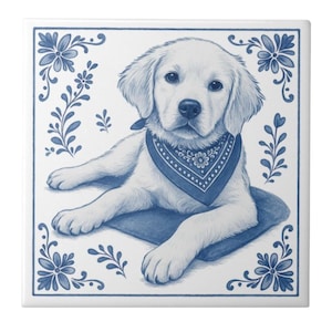 Könnte beinhalten: Quadratische, weiße Keramikfliese mit einer blau-weißen Illustration eines Golden Retriever-Welpen mit blauem Halstuch. Der Welpe liegt auf einem blauen Kissen. Die Fliese hat einen blauen Blumenrand.